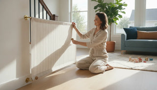 Parent installing a fabric safety gate between a wall and a wooden stairway banister in a bright contemporary home