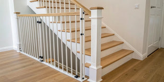 A stair gate installed at the bottom of stairs with y-spindles on a wooden banister.