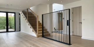 Stylish black metal indoor dog gate installed between a hallway and staircase.