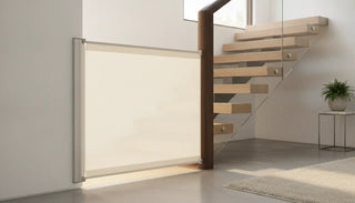 A premium fabric safety baby gate installed in a wall to banister configuration on a modern staircase